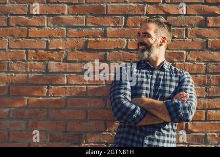 Portrait of modern businessman with beard standing in front of brick wall outdoor. Stock Photo