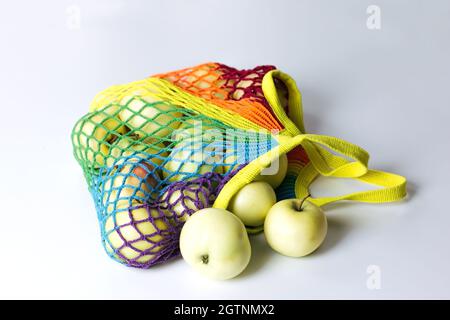 Reusable cotton string bag for shopping with green apples, multicolored rainbow LGBT trendy colors. It lies on a light table. The concept of zero wast Stock Photo