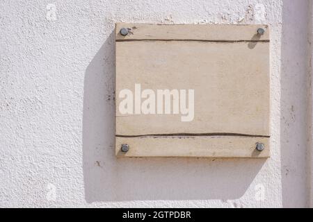 Sign plate mounted with screws on white wall. Blank label mockup, Wooden beige color empty board, business signage template, copy space. Stock Photo