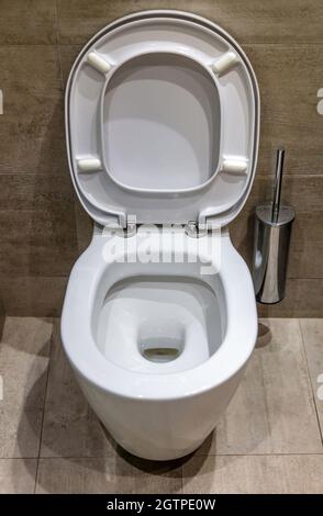 Modern toilet interior design, hanging white toilet bowl with open cover and brush. Luxury bathroom accessories on marble tiled walls and floor light Stock Photo
