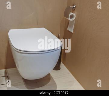 Toilet interior, ceramic white toilet bowl and black brush. Modern bathroom accessories on brown walls and tiled floor background. Stock Photo