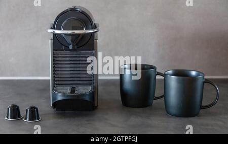 Coffee machine making espresso or cappuccino with pods. Black color machine, capsules and mugs on home kitchen table, front view Stock Photo