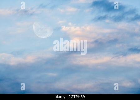 The Moon Is Rising In The Sky With Soft Clouds Set Against A Bright Blue Daytime Sky Stock Photo