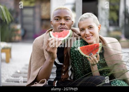 Multiracial couple eating watermelon in their yard Stock Photo