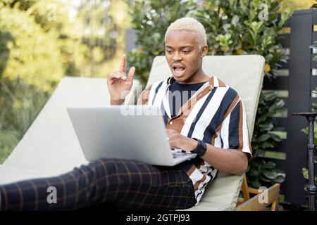 Black man using laptop on lounger at house garden Stock Photo