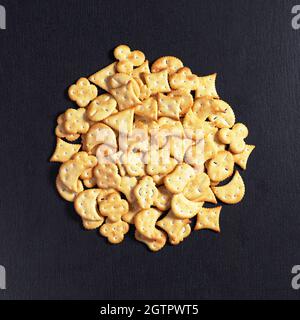 Heap of small crackers of different shapes on black stone background, top view Stock Photo