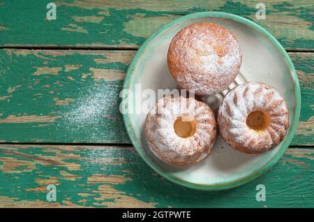 Tasty vanilla cupcakes sprinkled with powdered sugar in plate on old green wooden table, top view Stock Photo