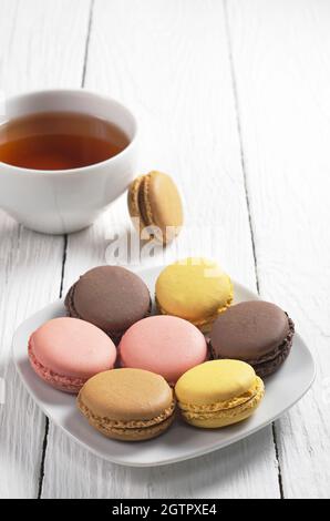 Macaroons in plate and a cup of hot tea on a white wooden table Stock Photo