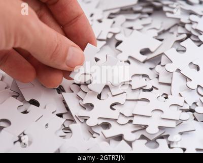 A woman holding a white puzzle piece above a pile of other white puzzle pieces. Close-up. Stock Photo