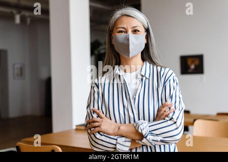 Confident woman office worker in face mask standing arms folded Stock Photo