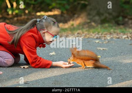 A girl with down syndrome feeds a squirrel nuts in the forest at sunset Stock Photo