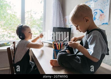 Two boy schoolkids brothers wearing headphones sitting near laptop at home. Back to school, Homeschooling, online study, home quarantine online Stock Photo