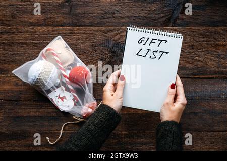 Christmas gift list, keeping track gifts christmas season. Female hands with open notepad and text Gift List on wooden background Stock Photo