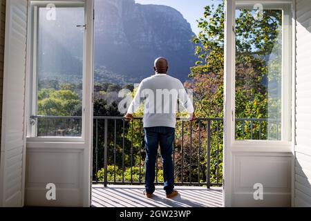 Back view of african american senior man standing on balcony and looking into distance Stock Photo