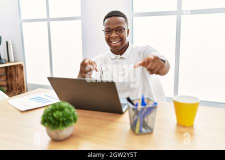 Young african man working at the office using computer laptop pointing to you and the camera with fingers, smiling positive and cheerful Stock Photo