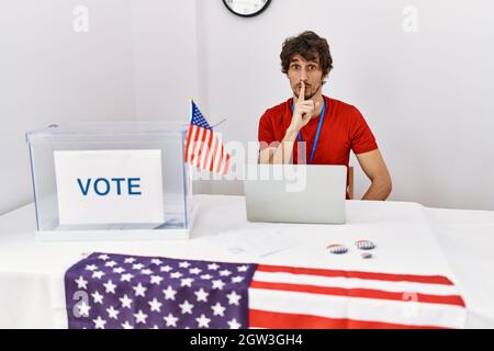 Young hispanic man at political election sitting by ballot asking to be quiet with finger on lips. silence and secret concept. Stock Photo