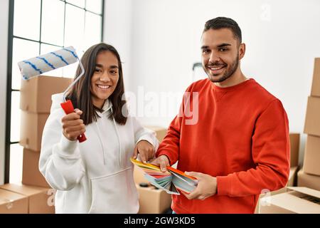 Young latin couple painting using paint roller at new home. Stock Photo