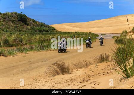 A group of people on motorbikes travelling through the giant Te Paki sand dunes in Northland, New Zealand Stock Photo