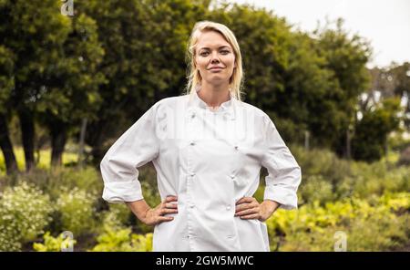 Confident female chef standing with her arms crossed on an organic farm. Self-sustainable young chef looking at the camera while standing in an agricu Stock Photo