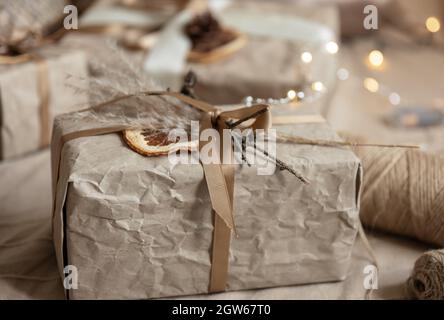 Close-up of a Christmas gift box, decorated with dried flowers and a dry orange, wrapped in craft paper. Stock Photo