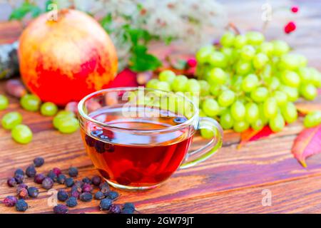 Infusion Of Hawthorn Fruit On The Background Of White Grapes, Pomegranates And Autumn Leaves