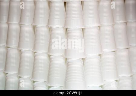 White plastic cups are seen stacked. Most disposable plastic utensils are made of polystyrene. Stock Photo