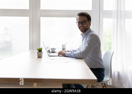 Portrait smiling businessman in glasses sitting at desk with laptop Stock Photo