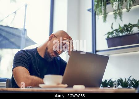 Tired young business man after long laptop pc work, having headache, feeling fatigue pain concept. Stock Photo