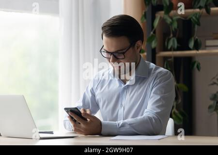 Smiling businessman in glasses using smartphone at workplace Stock Photo