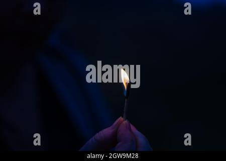 The flame of a small burning match in a woman's hands. Woman protects the fire from the wind. Dusk, shooting outdoors. Blur, noise, defocus, grain eff Stock Photo