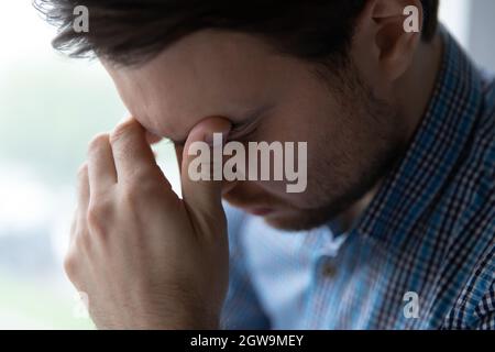 Close up depressed young man touching forehead, feeling headache Stock Photo
