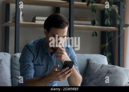 Thoughtful serious man touching chin, looking at smartphone screen Stock Photo