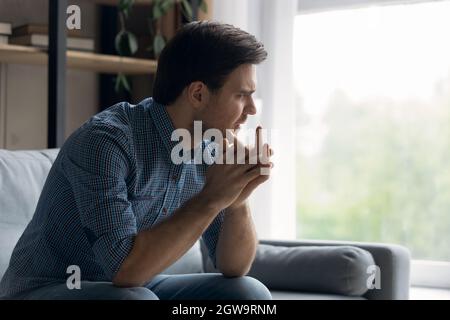 Unhappy thoughtful man looking in distance, sitting on couch Stock Photo