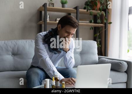 Unhealthy sick businessman sneezing, working on laptop at home Stock Photo