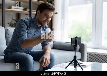 Smiling man showing thumb up, using smartphone on tripod Stock Photo