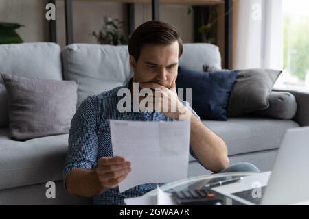 Thoughtful man checking financial documents, calculating bills, using laptop Stock Photo