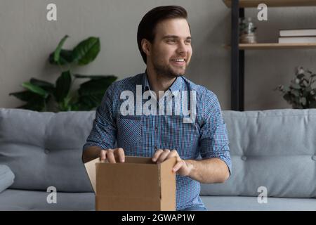 Overjoyed man holding cardboard box on laps, sitting on couch Stock Photo