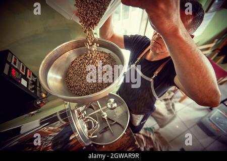 Man drip raw coffee over a coffee roasting machine. Stock Photo