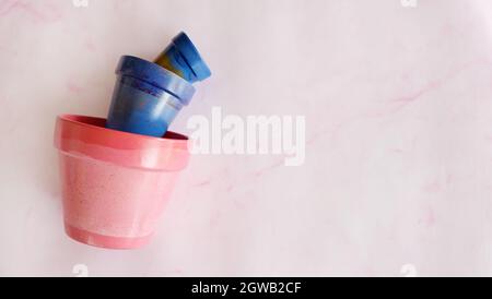 Flat lay of 3 terracotta pots in different sizes, from small to large. Pots are painted in blue and pink acrylic paints, and placed on pink background Stock Photo