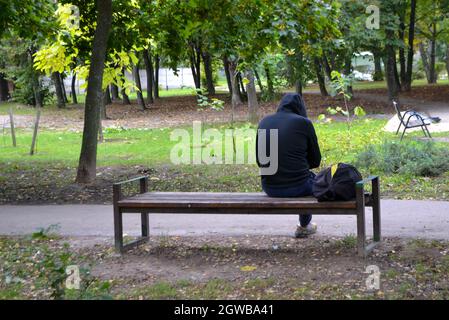 Young man in black jacket sitting alone on bench Stock Photo