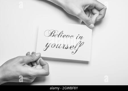 black and white photo of female hand holding a piece of paper with the inscription believe in yourself as a motivation Stock Photo