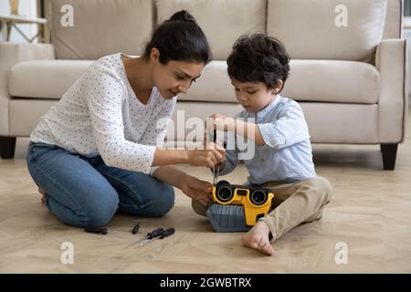 Happy young indian mother fixing toy car with little son. Stock Photo