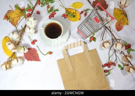 shopping card, paper bag and a coffee cup on a light marble background with natural autumn leaf decoration, seasonal holiday sale concept, copy space, Stock Photo