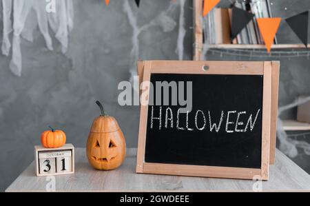 halloween text on black chalkboard wooden table with 31 october calendar and orange pumpkin. concept of happy halloween holiday atmosphere. Stock Photo