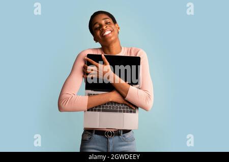 Portrait Of Happy Excited Black Woman Holding And Embracing Opened Laptop, Cheerful Pleased Young African American Lady Hugging Computer While Posing Stock Photo