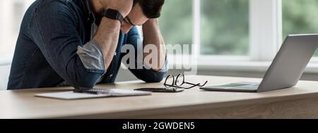 Deadline for freelancer. Tired unhappy young businessman holding head in hands upset about business failure, have headache or feel stressed about work Stock Photo