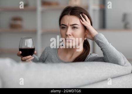 Drunk unhappy caucasian young woman with glass of wine suffering from depression and headache and relax at home, empty space. Alcoholic, social issue, Stock Photo