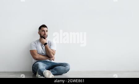 Young european bearded man, regrets something. Sad shocked unhappy pensive handsome guy sit on floor, think and suffering from depression and problems Stock Photo