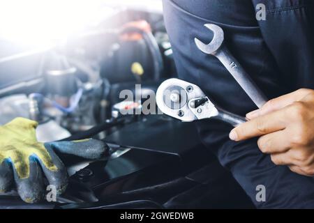 Car mechanic holding socket wrench and spanner in the auto repair garage with a engine compartment blurred on background. Maintenance service concept Stock Photo