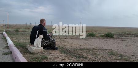 Young pensive male motorbike driver sits near road, enjoys good rest and wonderful nature view. Transport and lifestyle concept Stock Photo
